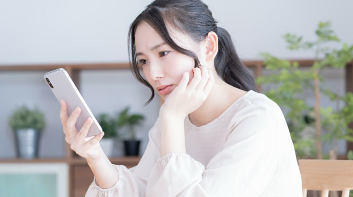スマホをもって悩む女性