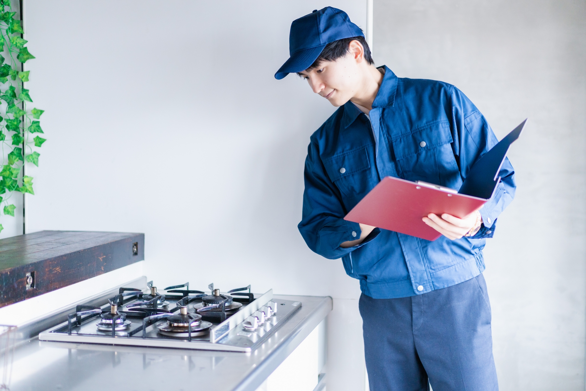 作業着を着た男性作業員が、クリップボードを手に、キッチンのガスコンロを点検している