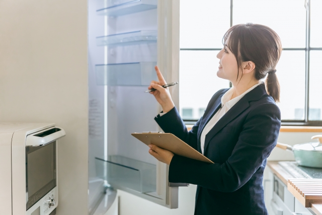 冷蔵庫の中を確認し、クリップボードにメモを取っている女性の写真