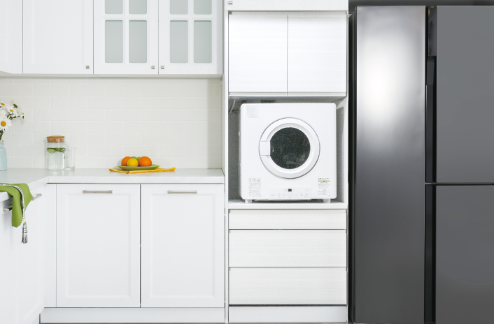 キャビネットの間に小型の衣類乾燥機が置かれ、その横に大型の冷蔵庫が並んでいる。