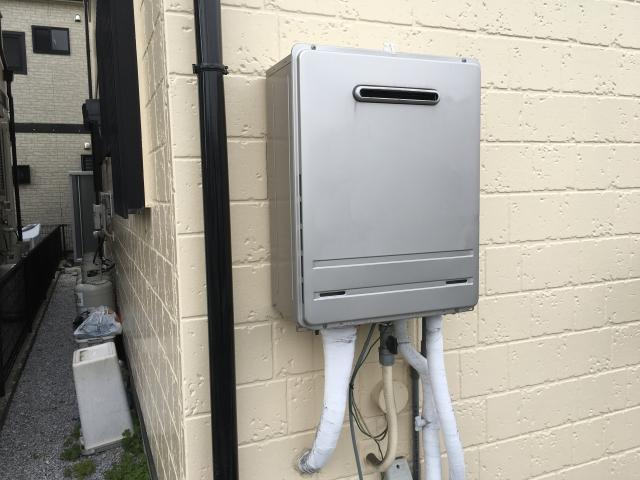 住宅の外壁に取り付けられた、シルバーの屋外壁掛型ガス給湯器。