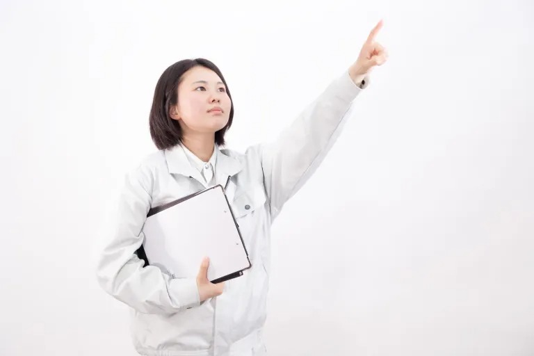 作業着を着てクリップボードを持ち、指差し確認する女性