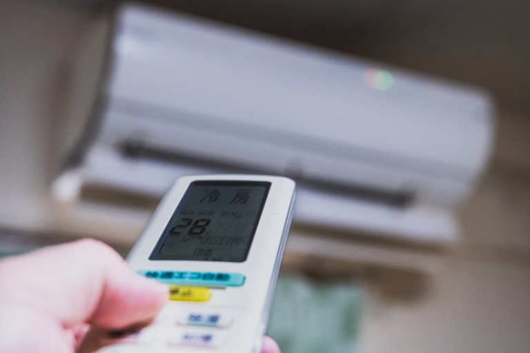 設定温度が28℃になっているエアコンのリモコンを操作する手元