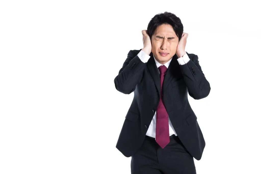 両手で耳を覆い、顔をしかめている、スーツを着た男性