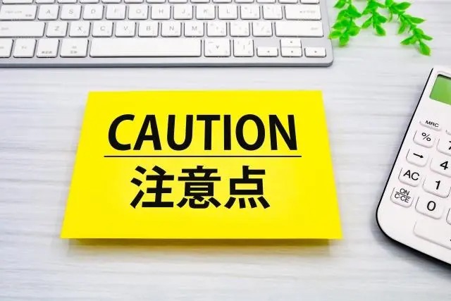 明るい木目調のテーブルの上に、大きく「CAUTION」「注意点」と黒文字で書かれた黄色いカード。上部にキーボード、右側に電卓と緑の葉が添えられている。