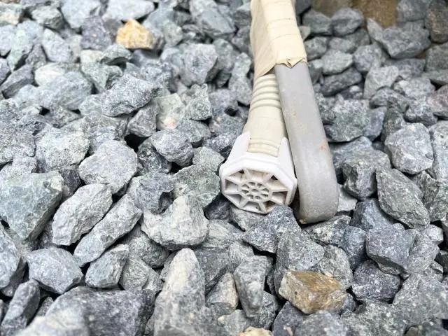 砂利の上に置かれたエアコンのドレンホースの先端に、白い樹脂製の防虫キャップが取り付けられている様子。隣にはエアコンの冷媒管が並んでいる。