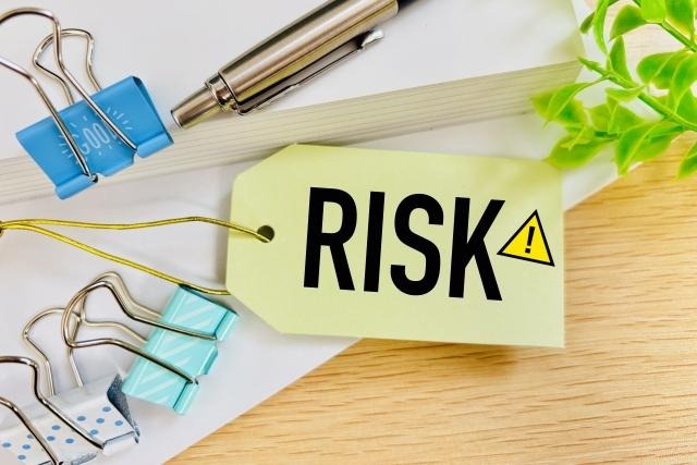 ノートやクリップが置かれたデスクの上に、「RISK」の文字と警告マークが描かれた黄色いタグが置かれている様子。