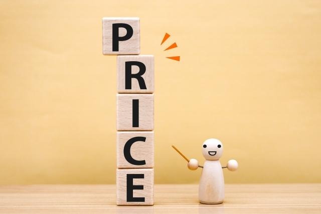 縦に積み上げられた「PRICE」の文字ブロックと、それを作業棒で指し示す小さな木製の人形。