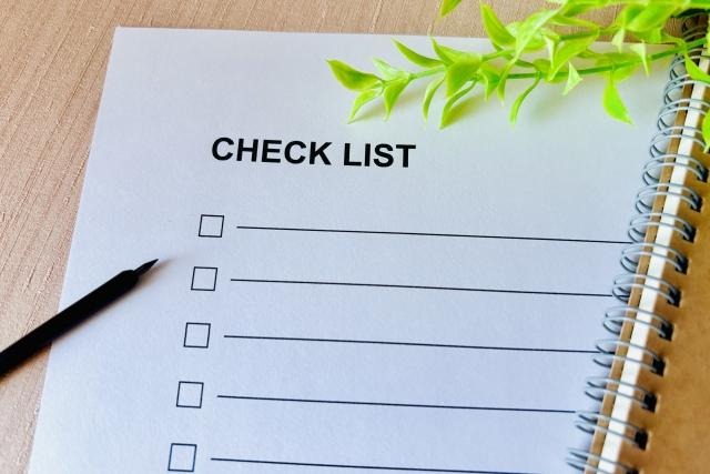 ノートの横に置かれた、「CHECK LIST」と印字されたチェックボックス付きの白い用紙と黒いペン。